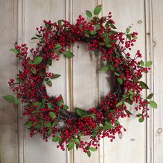 a wreath with red berries and green leaves hanging on a white wooden door, ready to be used as a christmas decoration