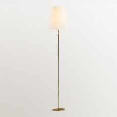 a gold floor lamp with a white shade on the top and bottom, standing against a wall