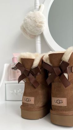 The UGG Bailey Bow boots are the perfect mix of cozy and cute. They have the same soft, warm feel as classic UGGs but with adorable bows on the back that make them stand out. Whether you’re running errands or just lounging, they keep your feet warm and add a stylish touch to any outfit. You get that classic comfort with a bit of extra flair! Brown Bow Ugg Boots, Outfits Ideas With Ugg Boots, Winter Boots Ugg, Coquette Ugg Boots, Uggs With A Bow, Ugg Boots Bailey Bow, Best Ugg Boots, Ugg With Bows, Cute Uggs Boots