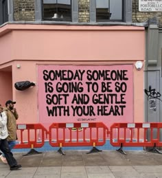 two people walking past a pink wall with writing on it