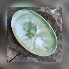 a green and white plate sitting on top of a piece of tree trunk with wood in the background