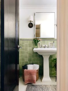 the bathroom is decorated in green tile and white fixtures, including a pedestal sink with a mirror above it