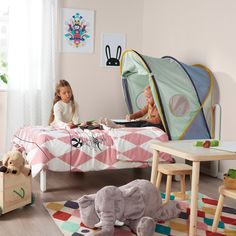 two children are sitting on a bed with an elephant and tent in the room behind them