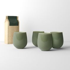 three green cups sitting next to each other on a white surface with a brown bag in the background