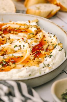 there is a plate of mashed potatoes with herbs on top and bread in the background