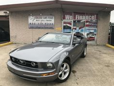 a gray mustang parked in front of a car dealership