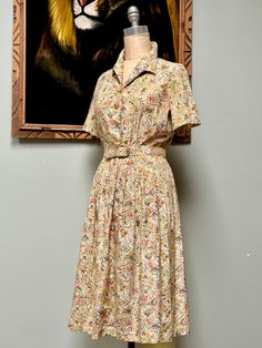 "For your consideration is a great vintage 1950's shirtwaist novelty print dress by \"Sears\". The print has a lot going on- there are Roman numerals in frames, buildings/houses, and urns with flowers. Shirtwaist dress style with pale yellow moonglow lucite buttons down the front, snap at the waist. Short sleeves, full skirt. The material feels like a silky acetate and has a nice sheen to it. Measurements: Size S 34\" bust 27\" max waist and belt to cinch smaller 9\" sleeve length 14\" shoulder 50s Shirt Dress, Vintage Mini Dress For Garden Party, 1950s House Dress, Vintage Collared Floral Print Dress, Early 1960s Fashion, 1950s Short Sleeve Cotton Dress, 1950s Cotton Buttoned Dresses, 1950s Shirtwaist Dress, 1940s Shirtwaist Dress