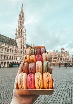 a hand holding a box full of macaroons in front of a large building