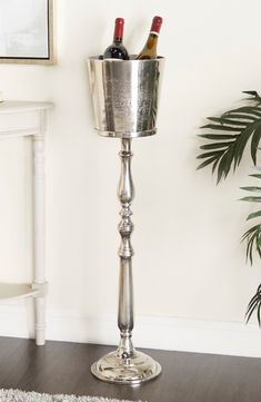 a tall silver candle holder with two wine bottles in it next to a potted plant