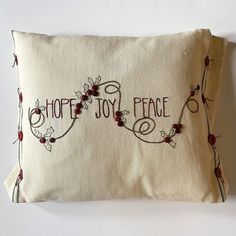 two embroidered pillows that say, shop joy peace and have red berries on the edges