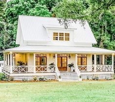 a white house sitting in the middle of a lush green field with lots of trees