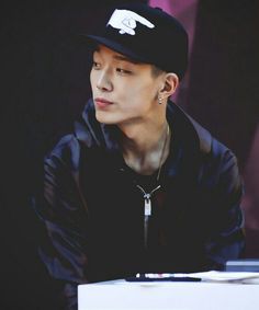 a young man wearing a black hat and jacket sitting at a table with a keyboard