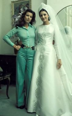 two women standing next to each other in front of a mirror wearing wedding gowns