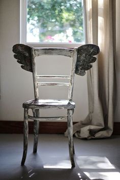 an old wooden chair sitting in front of a window with angel wings on it's back