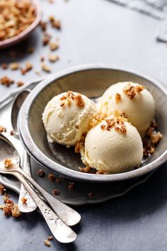 three scoops of ice cream are in a bowl with spoons on the side