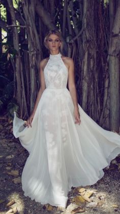 a woman wearing a white dress standing in front of trees