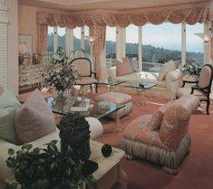 a living room filled with lots of furniture next to a window covered in pink curtains