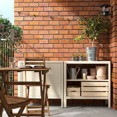 an outdoor table and chair with pots on it next to a brick wall that has a potted plant in the corner