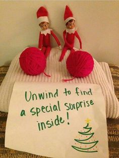 two elfs sitting on top of a bed next to a sign that says, unwind to find a special surprise inside