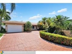 a driveway in front of a house with palm trees and shrubs around the entrance to it