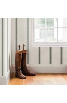 a pair of brown boots sitting on top of a wooden floor next to a window