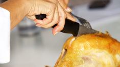 a person cutting up a turkey with a knife