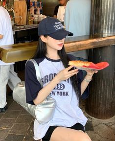 a woman sitting on the ground holding a slice of pizza in her hand and wearing a hat