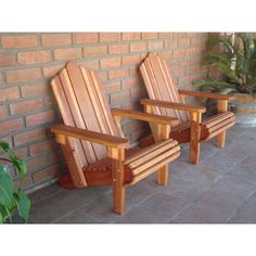 two wooden chairs sitting next to each other near a brick wall and potted plant