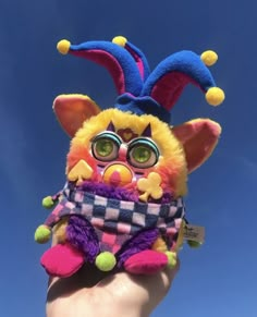 a hand holding up a stuffed animal wearing glasses and a hat with colorful decorations on it