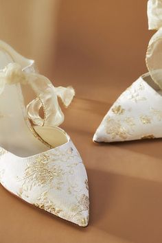 two pairs of white wedding shoes with gold lace on the toes and bows at the back