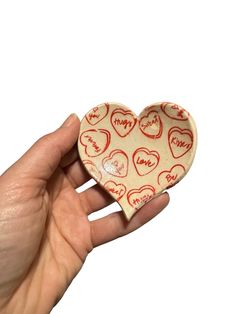 a hand holding a ceramic heart with many hearts on it