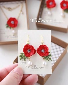 a hand holding a card with two red flowers and pearls on it in front of some jewelry