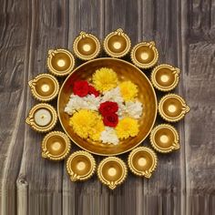 a golden plate with flowers and candles in it on a wooden table next to wood planks