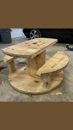 a table made out of pallet wood sitting on top of a cement floor next to a black car