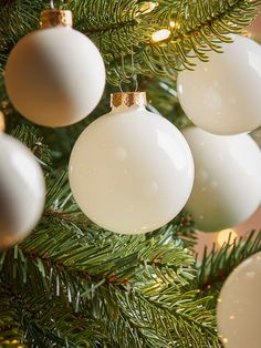 christmas ornaments hanging from the branches of a pine tree with gold and white baubles