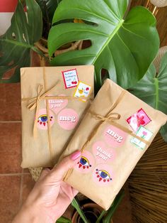 two packages with stickers tied to them sitting on a table next to a potted plant