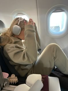 a woman sitting in an airplane with headphones on and looking out the window while listening to music