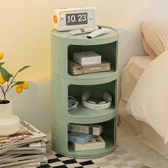 a stack of books on top of a green shelf next to a bed with yellow flowers