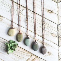 four necklaces with different colored stones hanging from them on a wooden table next to a plant