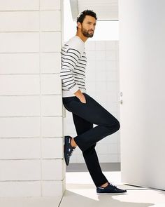 a man leaning against a wall with his feet on the ground and wearing black pants