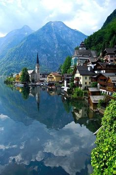 a lake with houses and mountains in the background, surrounded by greenery on both sides