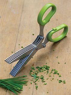 two green scissors are sitting on the table next to some chopped up herbs and chives