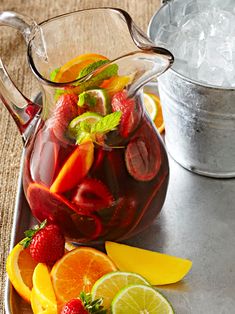 a pitcher filled with fruit sitting on top of a table next to an ice bucket