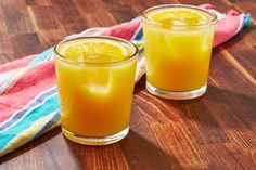 two glasses filled with orange juice sitting on top of a wooden table next to a towel