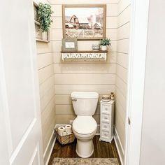 a white toilet sitting inside of a bathroom next to a wooden floor and framed pictures on the wall