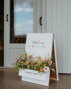 a welcome sign with flowers on it in front of a door