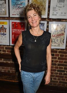 a woman standing in front of a brick wall with posters on the wall behind her