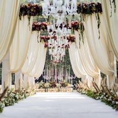 an outdoor wedding ceremony with white drapes and floral arrangements on the aisle, surrounded by greenery