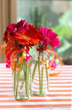 two vases filled with colorful flowers sitting on top of a striped tablecloth covered table