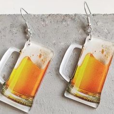 two beer mugs are hanging from silver earwires on a concrete surface,